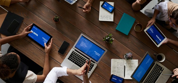 Overhead view of a diverse team discussing around a wooden table, using technology.